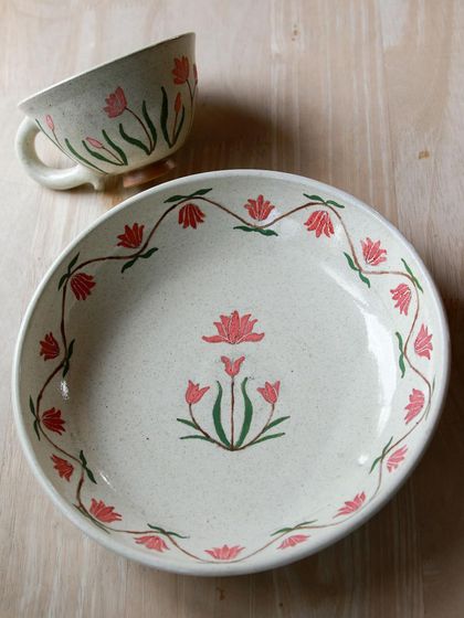 A beautifully hand painted plate and footed cup with delicate pink and green floral patterns, created by a student during their course.
