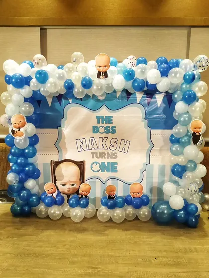 A Boss Baby themed photo wall for a first birthday, featuring a custom printed backdrop framed by a blue and white balloon structure.