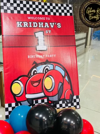 The welcome sign for Kridhav's race car party. The bright red sign with a cute cartoon car and checkered flag border gets guests excited for the "first lap" celebration.