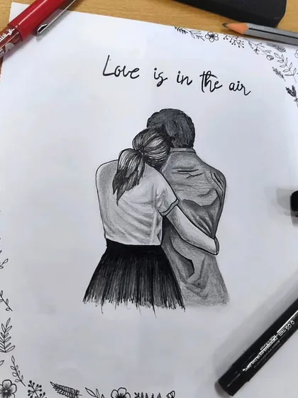 The couple sketch surrounded by my art supplies. This image gives a behind-the-scenes look at the tools I use, including fine-tipped pens and graphite pencils, to create your custom drawings.