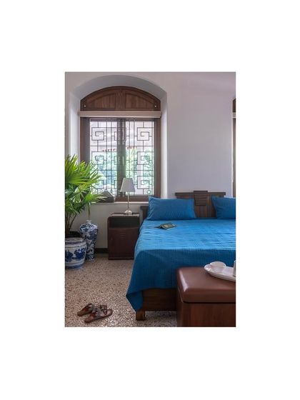 The master bedroom, where we paired a custom-designed bed with restored antique furniture. The original arched window with its intricate grillwork was preserved, maintaining the historical character of the room.