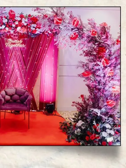 A reception stage decorated in shades of pink and purple, featuring a dramatic floral arch and a regal armchair for a touch of royal elegance.