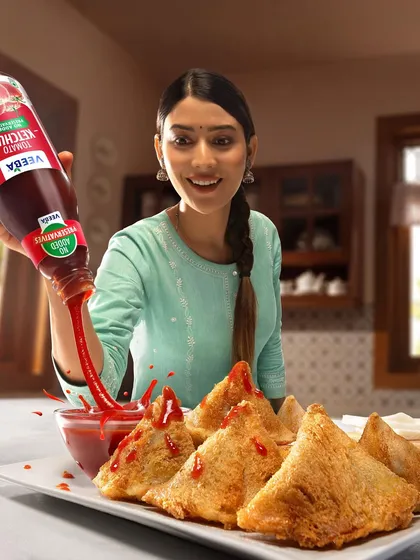 This action shot for Veeba's tomato ketchup campaign captures a perfect pour over a plate of hot samosas. The splash adds a dynamic element, making the familiar scene feel more energetic and appetizing.