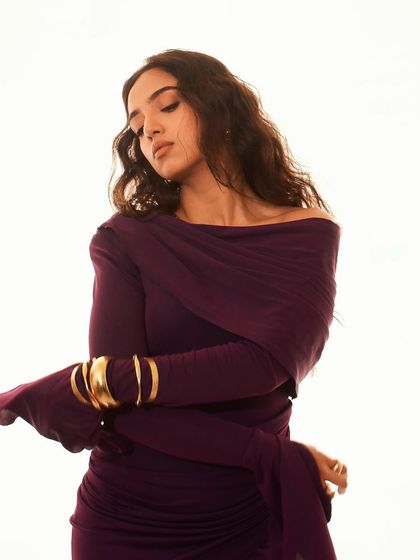 The bold gold cuff bracelet adds a strong, sculptural element to the soft, draped fabric of the purple gown, creating a beautiful contrast in this shot of Ahsaas Channa.