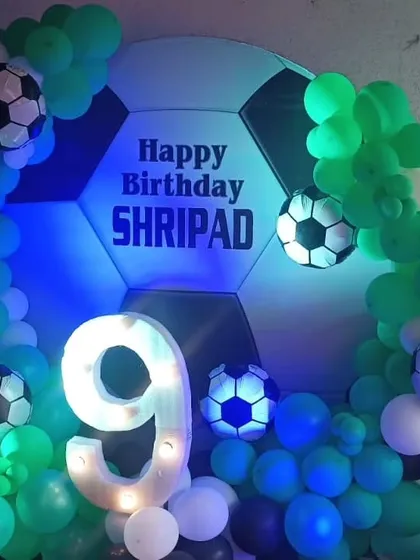 A birthday decoration for a football fan, featuring a giant football-shaped backdrop, a light-up number '9', and green and blue balloon arrangements.