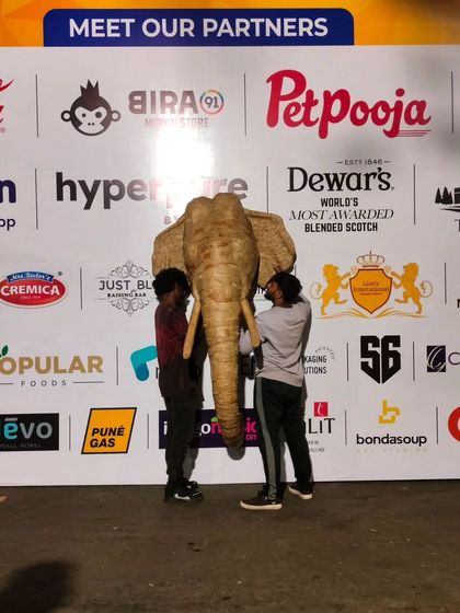 Taking our art on the road. Here, our team members are posing with the finished cardboard elephant head in front of a partner wall at an event, showing how our creations can serve as unique brand activations.