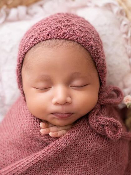 A sleeping baby in a cozy bonnet and wrap. The textures of the knitwear add a lovely, tactile element to the photograph.