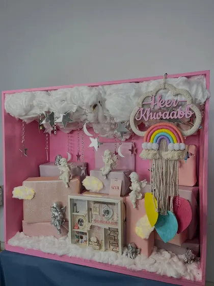 This angle highlights the depth and layering within the baby announcement box, with hanging crystals, fluffy clouds, and carefully placed gifts creating a three-dimensional effect.