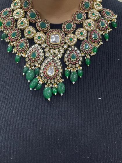 A heavy bridal necklace with a mix of kundan and polki stones, set in a traditional design with green stones and bead drops.