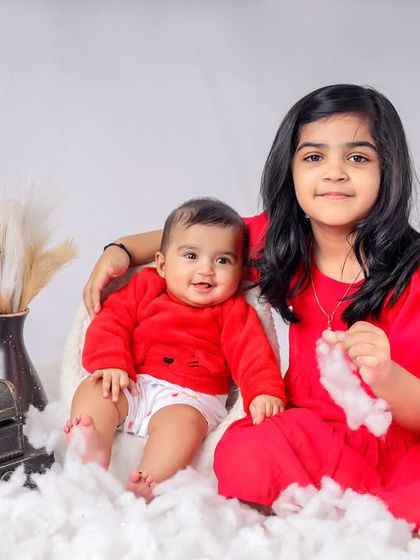 A delightful sibling portrait featuring an older sister and her baby brother. The festive red outfits and dreamy white cloud setup in our studio create a sweet and memorable photograph.