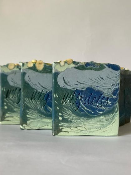 A lineup of our Mistletoe soaps, showing the beautiful wave-like design on top. The cool blue and green tones are inspired by frosty winter landscapes and the serene feeling of the holiday season.