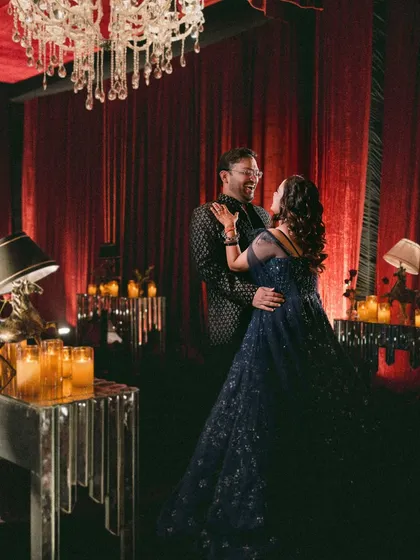 Komal and Pallav share a dance in a room filled with dramatic red curtains and warm candlelight, creating a romantic and cinematic sangeet portrait.