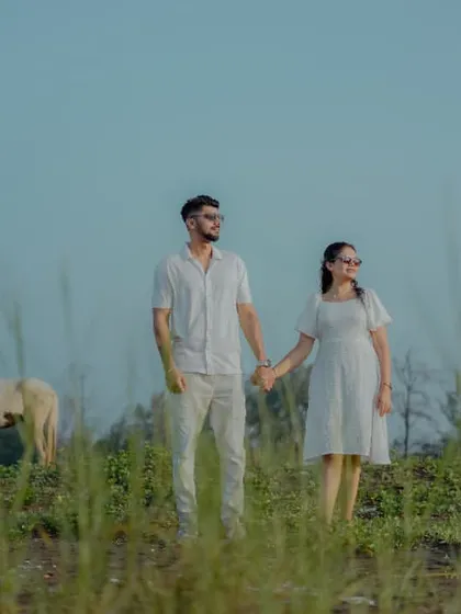 A wide-angle pre-wedding shot of a couple holding hands in a grassy field, with a horse in the background adding a rustic touch.