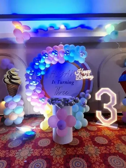 An ice cream themed third birthday party. The setup features ice cream cone props, a pastel balloon arch, and a light-up number '3'.
