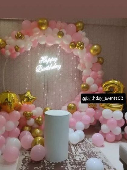 A classic pink and gold theme for a 20th birthday, featuring a balloon ring, neon sign, and matching foil numbers.