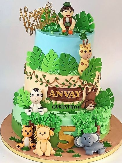 A grand three-tier jungle-themed cake for a 5th birthday. This adventurous cake is decorated with a variety of fondant animals, lush green leaves, and a fun, tiered design.