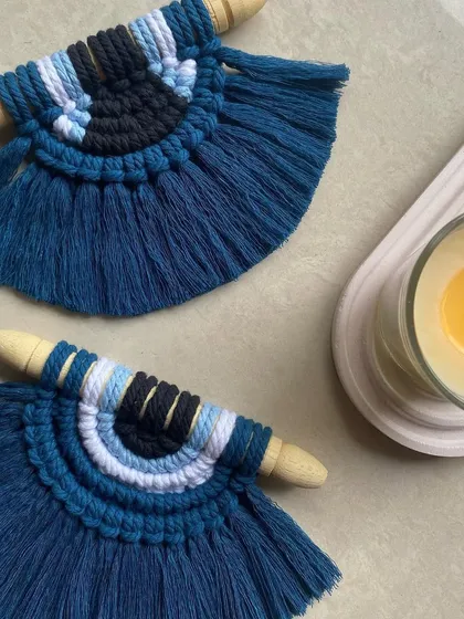 Two of our evil eye wall hangings styled with a candle. These handmade macrame pieces are designed to bring good vibes and a touch of boho decor to your home.