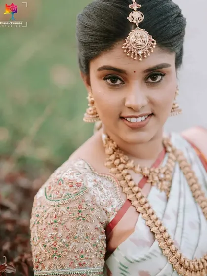 A classic close-up bridal portrait highlighting the intricate gold jewelry and the fine embroidery on her blouse. We focus on capturing the timeless beauty of a South Indian bride.