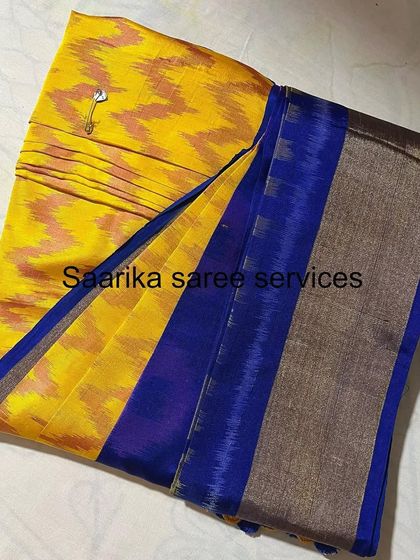 A yellow ikat saree with a blue border, pinned and folded. The pin ensures the pleats stay in place even during storage.