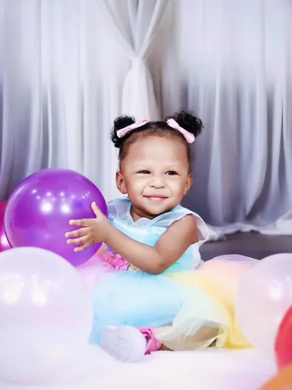A sweet moment with a one-year-old girl hugging a purple balloon during her birthday photoshoot.