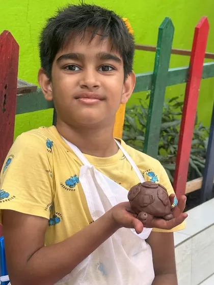 A young sculptor proudly showing off his handmade clay turtle. These workshops are designed to help kids turn their ideas into tangible masterpieces.