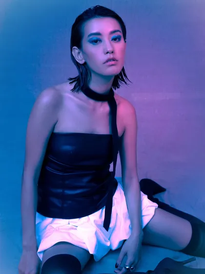A full-body shot from our neon-lit editorial. The combination of a leather top, white shorts, and thigh-highs creates a look that is both edgy and futuristic.