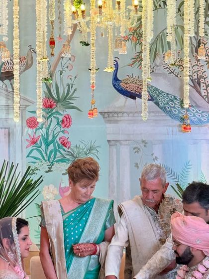 The bride and groom during their ceremony, framed by the beautiful Pichwai painting and delicate floral strings, creating a timeless and artistic memory.