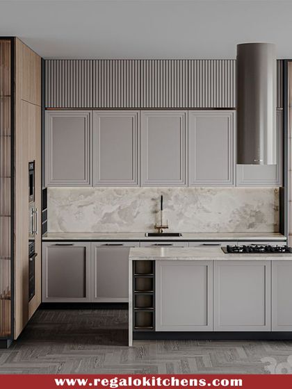 A sophisticated kitchen design with grey shaker cabinets and fluted glass tall units. The island hob is complemented by a sleek, cylindrical chimney. This kitchen perfectly balances classic and modern elements.