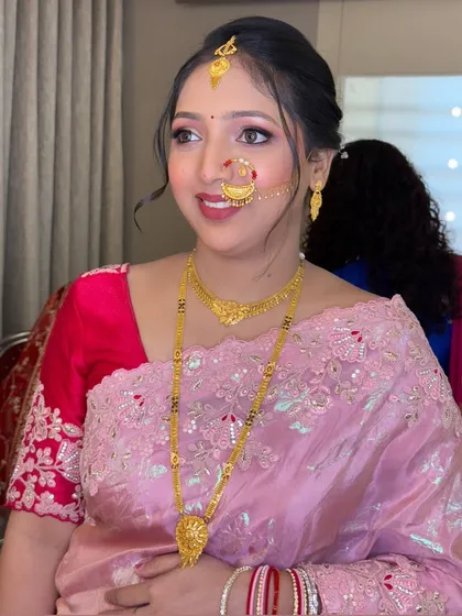 A beautiful traditional look for a wedding event, featuring a pink saree, gold jewelry, and a classic Maharashtrian nath.
