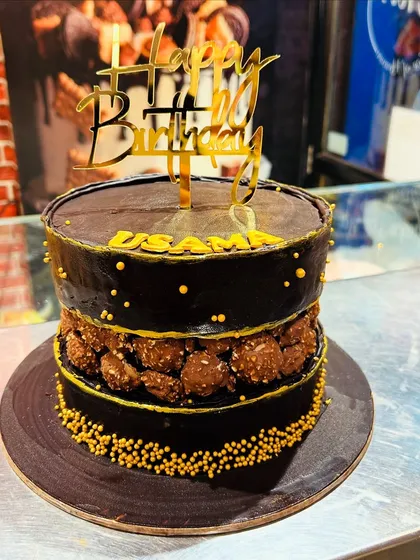 A decadent chocolate cake with a fault line filled with Ferrero Rocher chocolates, topped with a gold "Happy Birthday" sign.