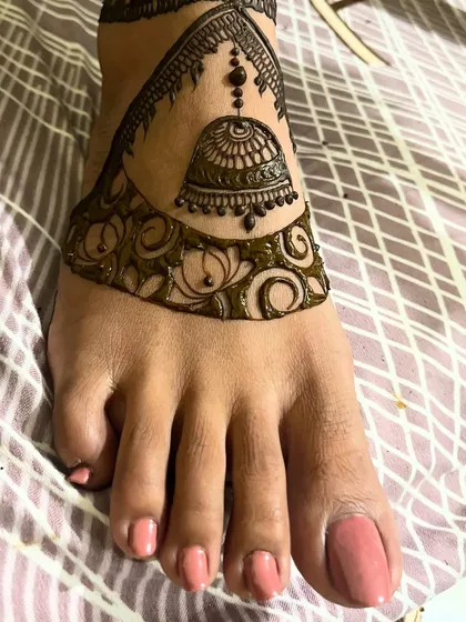 A beautiful cutwork design for the feet, featuring a hanging jhumka (bell) motif. This is the design with the henna paste still on, showing the bold, clean lines.