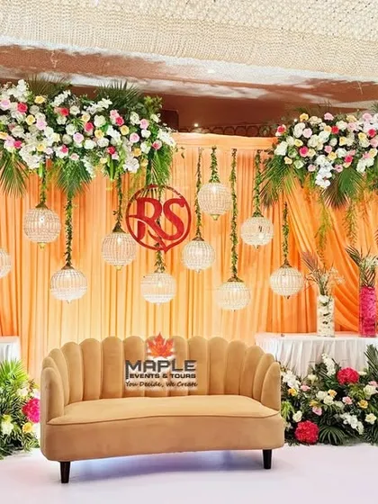A warm and inviting stage design with peach-colored drapes and lush floral arrangements. The hanging globe lights and a custom monogram for the couple add a personalized and intimate touch to the celebration.