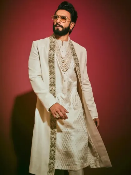 An off-white layered sherwani look, inspired by celebrity fashion. The outer jacket has embroidered lapels, worn over a textured kurta with a pearl necklace.