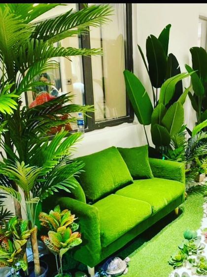This cozy corner is filled with various artificial tropical plants, including palms and birds of paradise, surrounding a bright green sofa to create a lush, indoor jungle vibe.