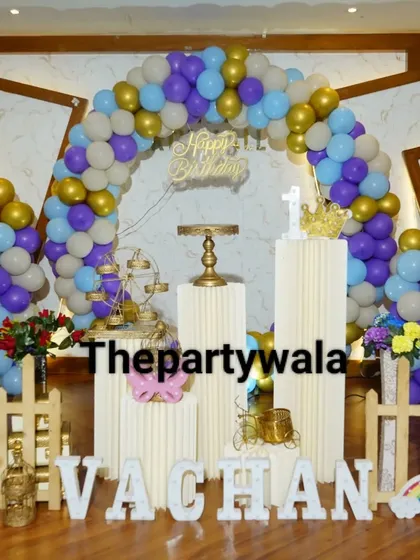 Another view of the purple, blue, and gold balloon arch, showing the full setup with the picket fence and props.