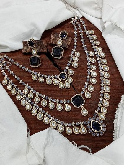 A grand, three-layered AD necklace set. This piece is designed for maximum impact, featuring square and teardrop stones, and is available in blue, green, pink, and red.