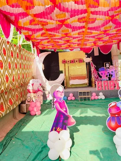 A wide view of the baby shower pandal, showing the stage and aisle decorated with character cutouts.