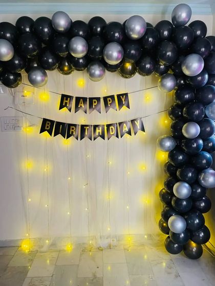 A black and silver balloon arch against a fairy light curtain, creating a simple and elegant backdrop.