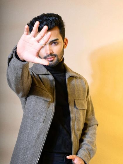 A modern, confident pose of a model in a grey felt jacket over a black turtleneck. The direct gaze and gesture create an engaging and bold look for a contemporary menswear brand.