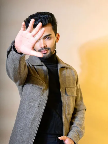 A modern, confident pose of a model in a grey felt jacket over a black turtleneck. The direct gaze and gesture create an engaging and bold look for a contemporary menswear brand.