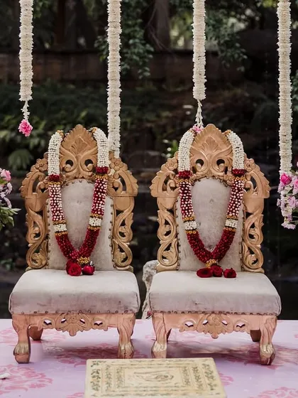 Ornate golden chairs for the bride and groom at the mandap, decorated with red rose garlands.