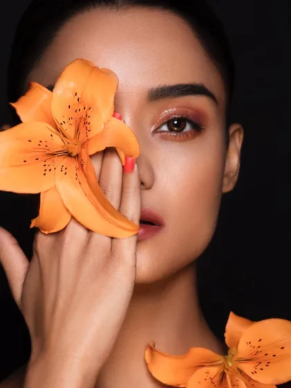 A warm, orange-toned eyeshadow look complemented by a beautiful orange lily. This shows a sophisticated use of color theory.
