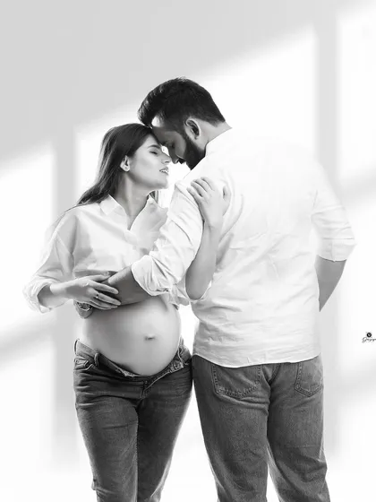 An intimate black and white portrait of a couple in a gentle embrace. The casual outfits and soft lighting create a timeless and authentic image of their connection.