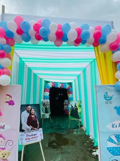 A vibrant entrance tunnel for an outdoor baby shower, decorated with pink, blue, and white balloons and gender-themed banners.