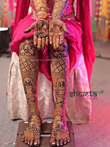 The complete bridal mehendi look. This photo showcases the intricate designs on both the palms and the full length of the legs, featuring beautiful peacock and jaali work.