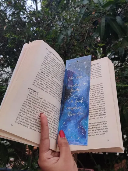 Here is one of my galaxy-themed bookmarks in action. This piece, featuring a hand-lettered quote about finding ourselves in books, is designed to be a beautiful companion for your reading adventures.
