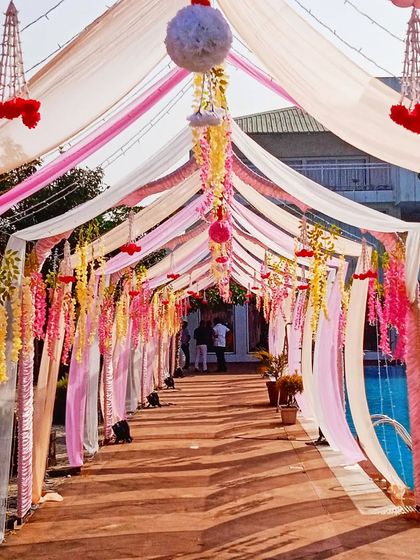 A festive poolside walkway decorated with a canopy of pink, white, and yellow drapes and hanging floral strings, perfect for a day wedding.