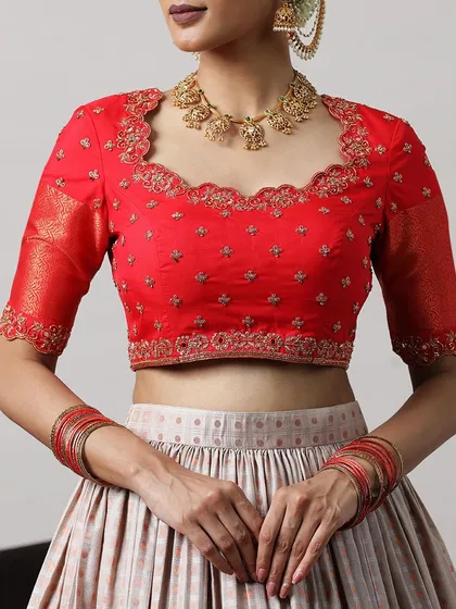 A close-up of the red blouse, featuring a scalloped neckline and delicate embroidery, paired with a statement gold necklace.