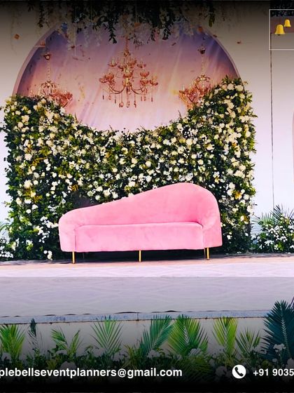 A romantic reception stage with a pink chaise lounge set against a backdrop of white flowers and elegant chandeliers, perfect for a fairytale celebration.