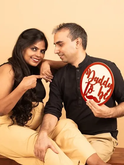 A playful studio shot where the mom-to-be points to her partner, who holds a 'Daddy to be' sign. It’s a fun way to announce the exciting news.